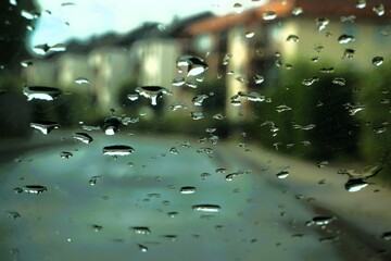 Abstraktes Motiv mit Wassertropfenmuster vor Kleinstadtpanorama mit Straße, Gehweg und Häusersiedlung bei Regen am Nachmittag im Frühling