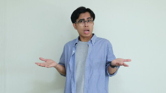Young Asian man making an "I don't know" gesture in a studio setting. Confused or uncertain expression, suitable for concepts like doubt, misunderstanding, or decision-making