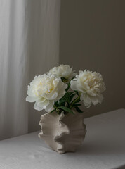 Bouquet of white peonies in a creative ceramic vase on the table