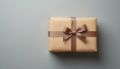 A neatly wrapped gift box, tied with a brown satin ribbon, sits on a grey background surface.
