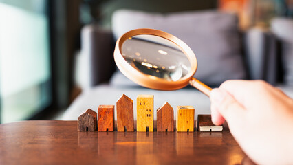 Hand holding magnifying glass and looking at house model, house selection, real estate concept.