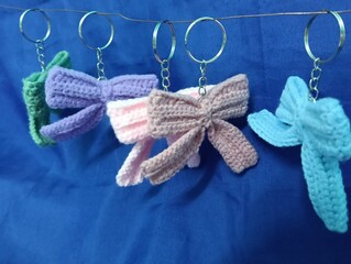 Many  handmade crochet keychains featuring bow designs in pastel color hanging on blue  fabric...