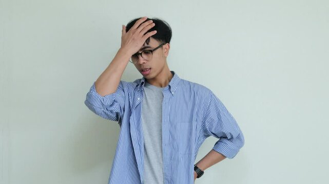 Young Asian man slapping his forehead with a regretful expression in a studio setting. Captures frustration or self-blame, perfect for emotional or advertisement vidios