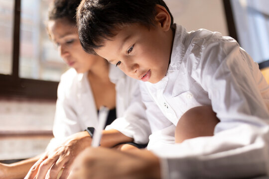Focused asian boy drawing next to his mother at home