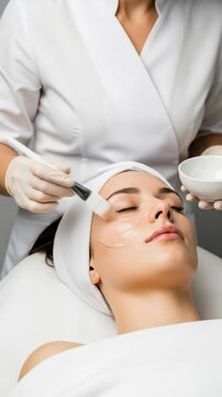 Woman receiving facial treatment from cosmetologist applying clear gel mask on face. Beauty spa clinic skincare procedure footage.