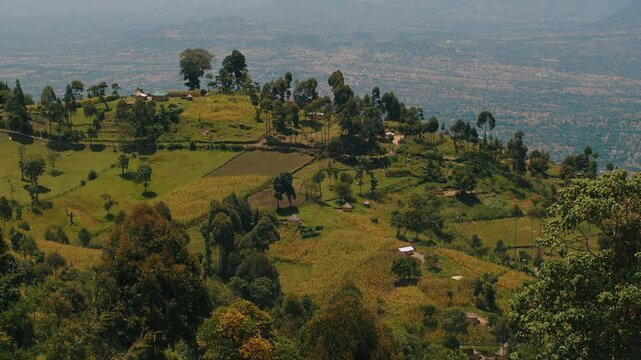 Panorama of hazy mountain peaks and the Great Rift valley with scattered on it buildings. Typical Kenyan bomas houses.