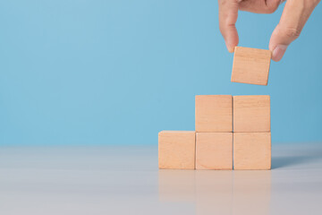 Hand arranges blank blocks for idea development or design structure. Blue background adds modern tone.
