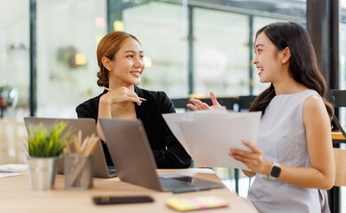 Two Asian company employees and colleagues teamwork discussing  together in the office. by talking and giving advice to each other
