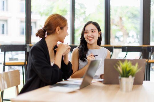 Two asian business women in teamwork discussing and using laptop in the office . Two excited happy asian business women are talking and consulting.
