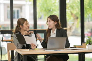 Two Asian businesswomen sitting in a meeting, working on a table, with laptops, chart documents,...