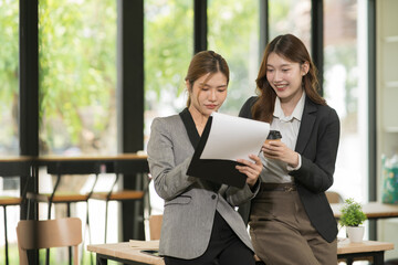 Obraz premium Two Asian businesswomen sitting in a meeting, working on a table, with laptops, chart documents, consulting on investment and financial business.