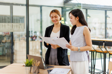 Asian Two young business women Standing talking together in modern office workplace, looking at...