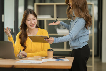 Two Asian businesswomen using laptops, on the table there are graph documents working on business investment.