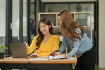 Two Asian businesswomen using laptops, on the table there are graph documents working on business investment.