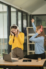 Asian woman wearing headphones standing and dancing celebrating, showing her appreciation, joy, office room