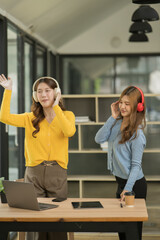Asian woman wearing headphones standing and dancing celebrating, showing her appreciation, joy, office room