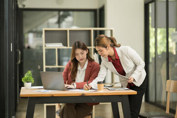 Two Asian businesswomen using laptops, on the table there are graph documents working on business investment.