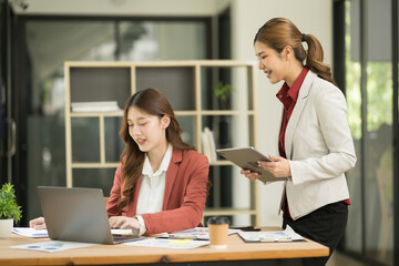 Two Asian businesswomen using laptops, on the table there are graph documents working on business investment.