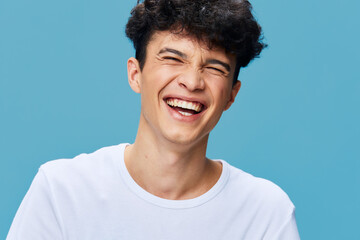 Laughing man with curly hair wearing white t-shirt against blue background, showing joyful...