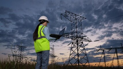 Utility worker standing under power pylons, Professional analyzing electric towers, Fieldwork by energy specialist, Safety helmet and high visibility, Wireless data collection on the go, Engineer - Powered by Adobe