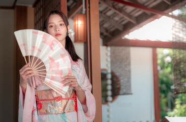 Fototapeta premium Young Woman in Traditional Kimono Holding a Folding Fan Outdoors