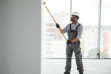 African man paints a white wall with a roller. Repair of the interior