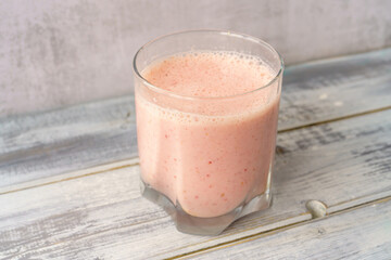 Fresh pink smoothie in clear glass on light gray wood background. Healthy refreshing drink for wellness and nutrition concept. Natural and organic beverage.