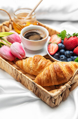 Romantic breakfast in bed with coffee, croissants, berries, honey and tulips