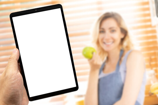 Mockup Tablet with Blank Screen in Kitchen, a blur smiling Woman Holding Green Apple in Background. Ideal for concepts related to healthy lifestyle, cooking apps, or modern technology at home.