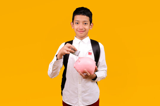 Smiling Young Student With Backpack Inserting Money Into Pink Piggy Bank Over Yellow Background
