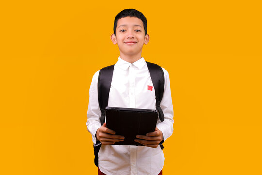 Cheerful Young Asian Student Boy With Backpack Holding Digital Tablet Isolated On Yellow Background