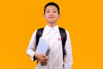 Confident Young Asian Student Boy With Backpack And Notebooks Isolated On Yellow Background