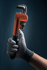 Plumbers hand in glove holding a pipe wrench on blue background.
