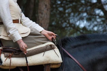 Detail of a woman's hand holding the riding crop and reins of her black purebred Spanish horse in a...
