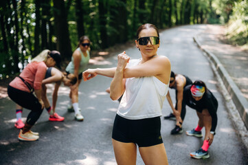 Woman in sunglasses is standing. Group of runners are together outdoors