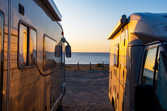 Two motorhomes bathed in early morning sunlight at a beach in Spain. Camper and motorhome holiday image. Camping car. Hymer.