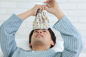 ベッドで体温を測るパジャマ姿の男性