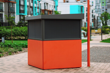 urban kiosk in modern residential area features sleek red and gray design. surrounded by greenery...