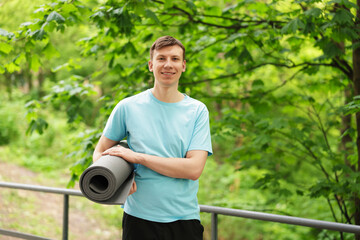 Young man with yoga mat in park