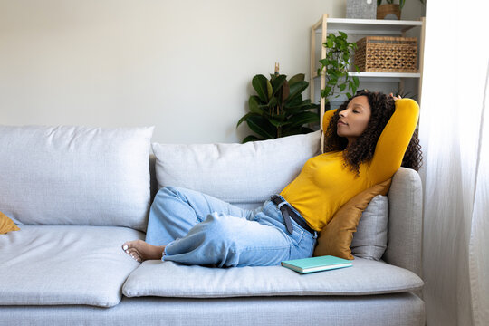 Side view of African American woman relaxing on the couch at home living room. Copy space.