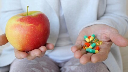 Doctor showing red and yellow apple and colorful pills in two hands, choosing between natural and chemical medicine for health and disease treatment