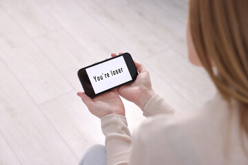 Cyber bullying. Upset teenage girl looking at smartphone with text You Loser at home, closeup