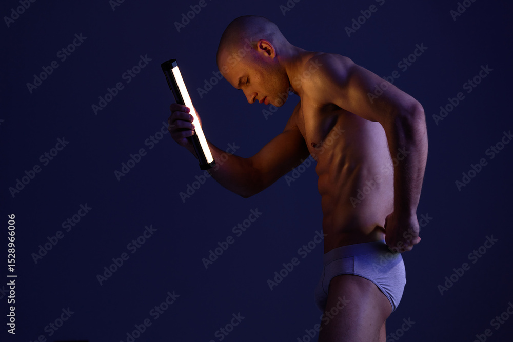 Poster athletic man posing with a light in a dark setting, showcasing emotion and strength. this image capt