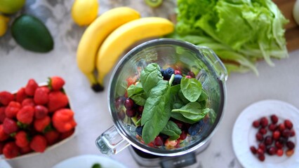 Blending fresh spinach, cranberries, blueberries, bananas, strawberries, avocado, lemon, and lettuce into a nutritious smoothie for a healthy lifestyle