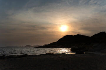 Sun setting behind rocky coastline creating golden reflection on water
