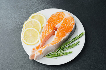 Raw salmon steak with lemon slices and rosemary on white plate over light background
