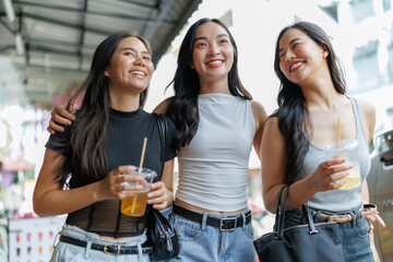 Fototapeta premium Three asian women walking and smiling together while drinking fruit juice