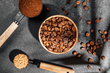 Ground coffee, instant coffee and beans in scoops and wooden bowl on dark background