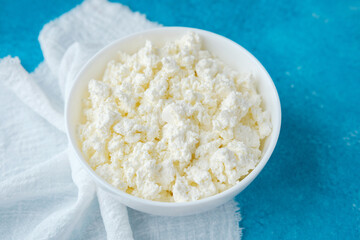 bowl of fresh cottage cheese on blue background with white napkin