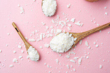 Multiple wooden spoons with soy wax flakes on pastel pink background